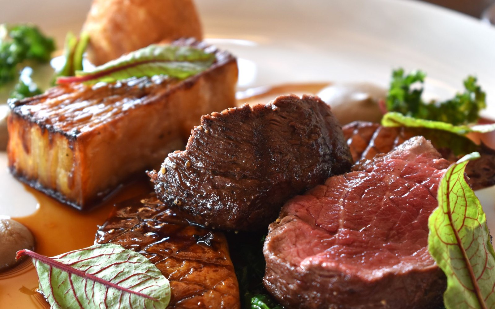 A cross-section of braised beef cheek, plated whole in its reduced, glossy sauce